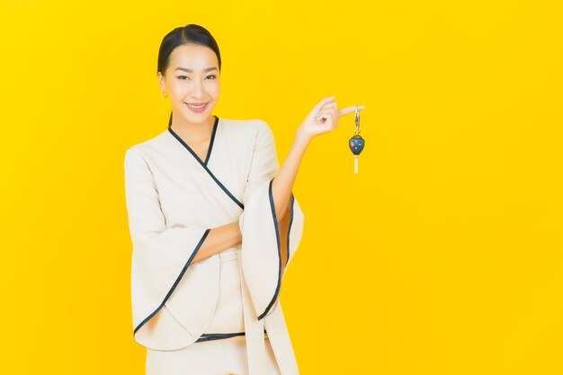 Portret van mooie jonge bedrijfs Aziatische vrouw met autosleutel op gele muur