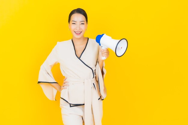 Portret van mooie jonge bedrijfs Aziatische vrouw met megafoon voor mededeling op gele muur