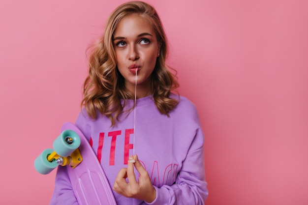 Gratis foto portret van mooie jonge dame in vrijetijdskleding. indoor portret van mooie blonde meisje met skateboard geïsoleerd op pastel.