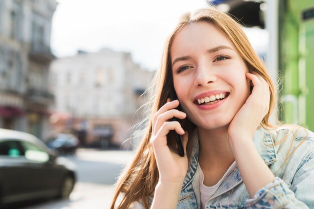 Portret van mooie jonge glimlachende vrouw die op cellphone spreekt