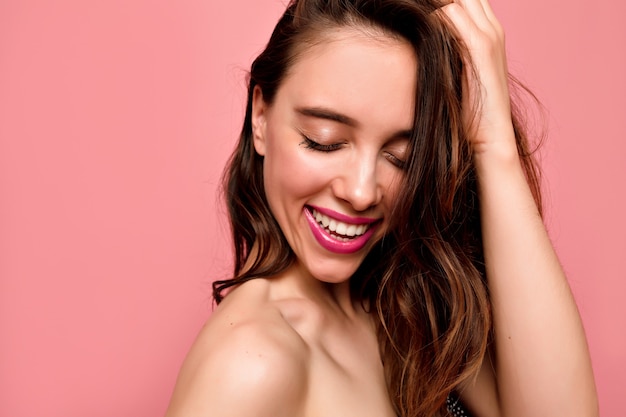 Portret van mooie jonge lachende vrouw met witte tanden en roze lippen met gesloten ogen op roze muur close-up