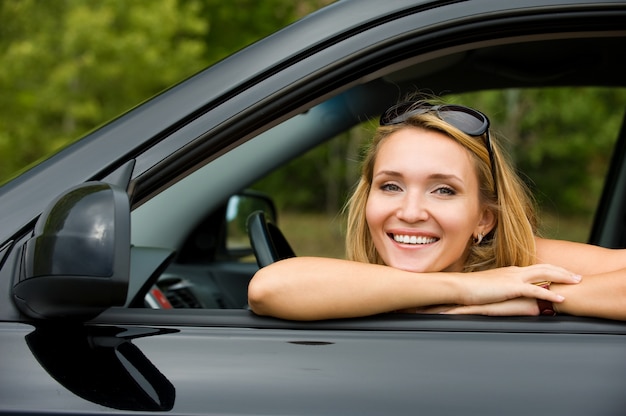 Portret van mooie jonge vrolijke vrouw in de nieuwe auto - buitenshuis