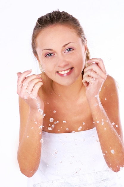 Portret van mooie jonge vrouw die haar gezicht bespattend water wast, het glimlachen