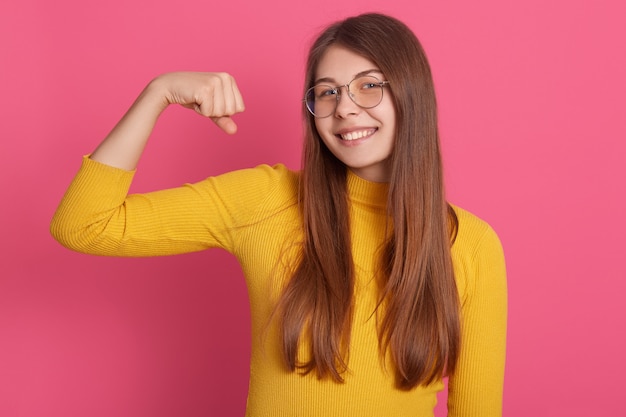 Portret van mooie jonge vrouw in gele casual kleding. Schitterend vrouwelijk model die over roze muur glimlachen,