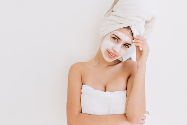 Portret van mooie jonge vrouw met handdoeken na bad nemen cosmetisch masker op haar gezicht.