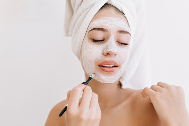 Portret van mooie jonge vrouw met handdoeken na bad nemen cosmetisch masker op haar gezicht.