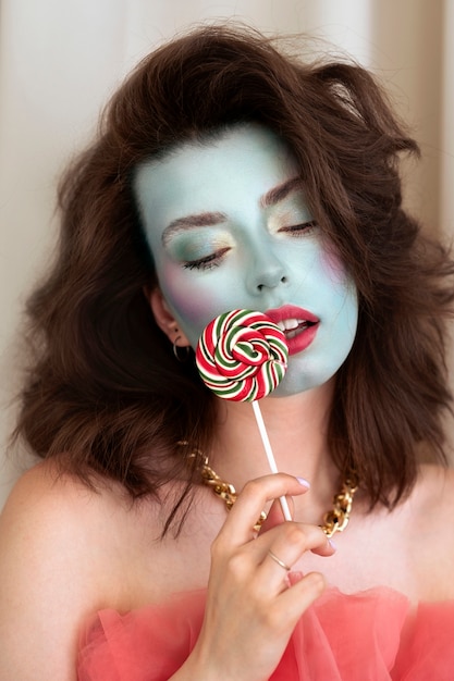 Gratis foto portret van mooie jonge vrouw met kleurrijke gezichtsmake-up en lolly