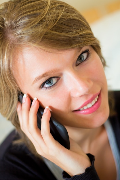 Portret van mooie jonge vrouw thuis met mobiel.