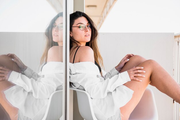 Portret van mooie jonge vrouw zittend op de stoel tegen reflecterend glas