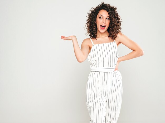 Portret van mooie lachende model met afro krullen kapsel gekleed in zomer hipster kleding. Vrouw demonstreren iets op haar hand