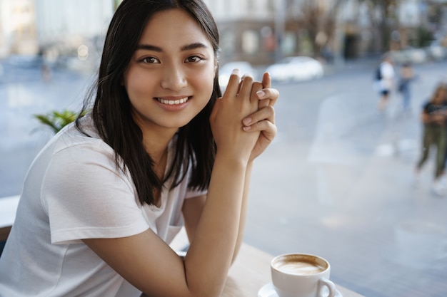 Portret van mooie natuurlijke vrouw koffie drinken in café alleen, zittend in de buurt van raam, glimlachend op camera gelukkig.