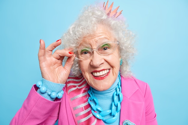 Portret van mooie oudere grijsharige vrouw houdt hand op de rand van de bril en glimlacht vrolijk