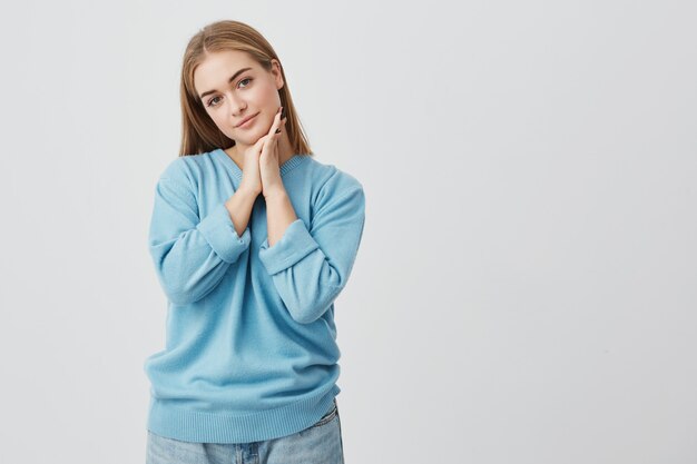 Portret van mooie, tedere, charmante europese vrouw met rechte blonde haren dragen van casual kleding kijken met rustige en doordachte expressie, met haar handen onder haar kin.