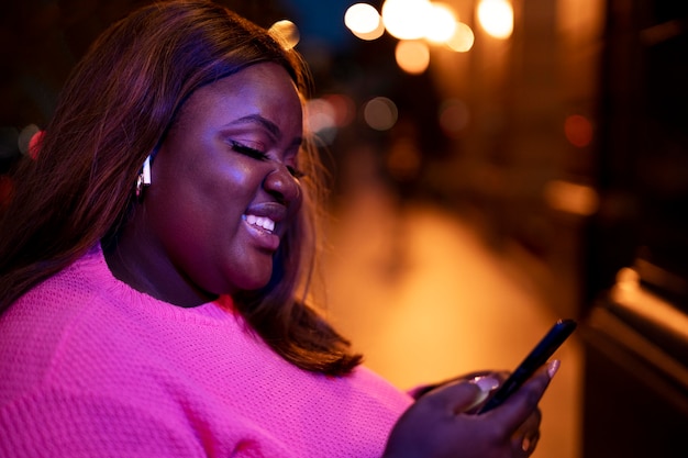 Gratis foto portret van mooie vrouw die 's nachts smartphone gebruikt in de stadslichten