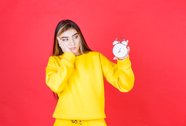 Portret van mooie vrouw die tijd op klok op rode muur bekijkt