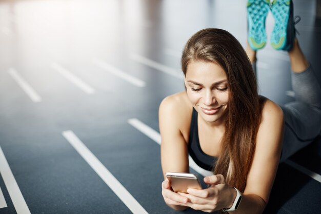 Portret van mooie vrouw met behulp van mobiele telefoon en fitnesstracker in de sportschool om haar gewicht en verbrande calorieën bij te houden. Gezond leven concept.