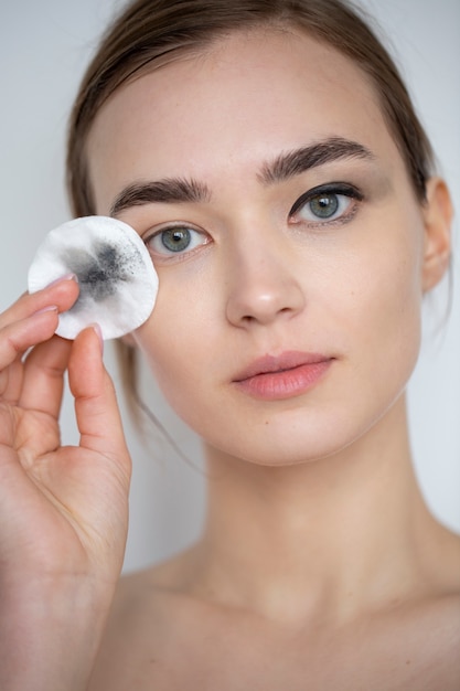 Portret van mooie vrouw met heldere huid die make-up remover pad gebruikt voor haar oogmake-up