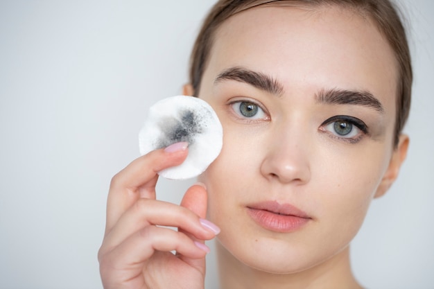 Portret van mooie vrouw met heldere huid die make-up remover pad gebruikt voor haar oogmake-up