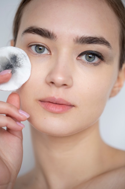 Gratis foto portret van mooie vrouw met heldere huid die make-up remover pad gebruikt voor haar oogmake-up