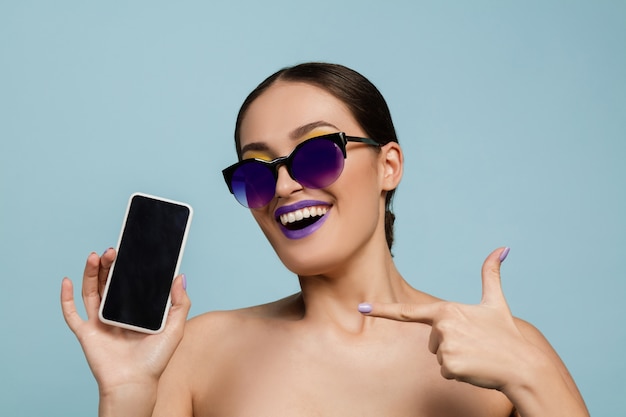 Portret van mooie vrouw met lichte make-up en zonnebril op blauwe studio