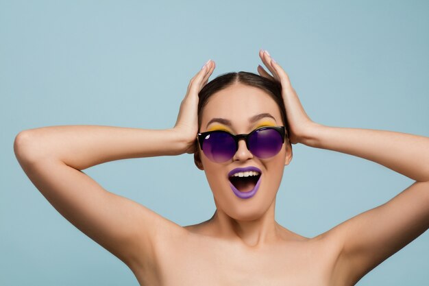 Portret van mooie vrouw met lichte make-up en zonnebril op blauwe studio