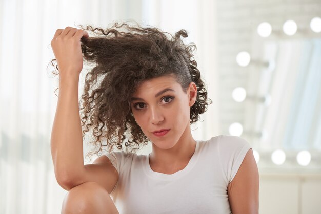 Portret van mooie vrouw wat betreft haar krullend haar dat camera bekijkt