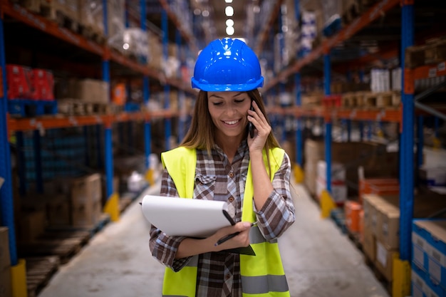 Portret van mooie vrouwelijke magazijnmedewerker met gesprek op mobiele telefoon in groot distributiecentrum voor opslag