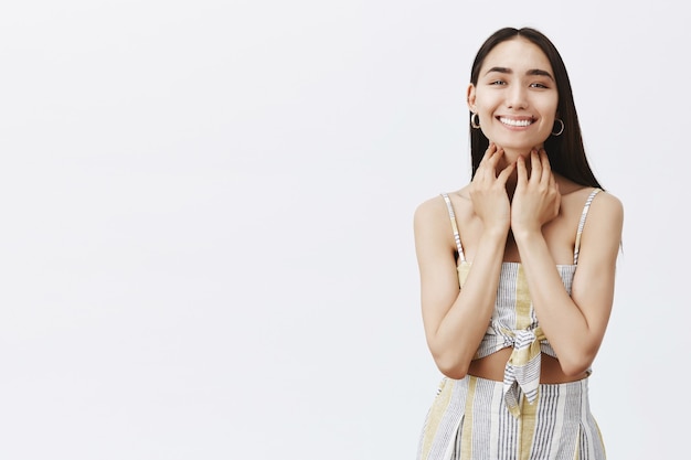 Portret van mooie zorgeloze en vrolijke vrouw die breed glimlacht na het zien van de resultaten van de cosmetologische procedure, het verzorgen van de huid over de grijze muur