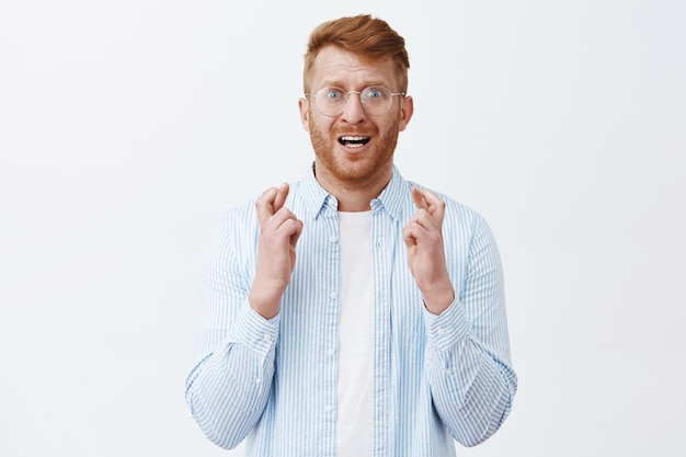 Portret van nerveuze en intense mannelijke roodharige man met borstelharen in transparante glazen, vingers kruisen en fronsen terwijl hij angstig hoopt dat er iets gebeurt