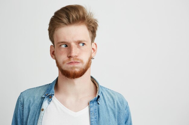 Portret van nerveuze jonge mens met baard die het overhemd van Jean draagt dat kant bekijkt.