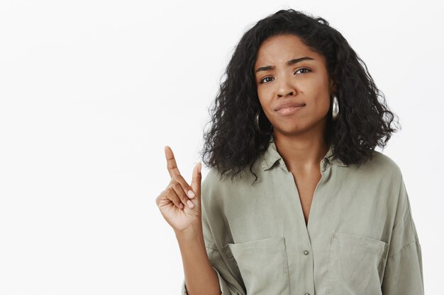 Portret van niet onder de indruk ontevreden onhandige schattige Afro-Amerikaanse vrouw in blouse grijnzende en grinnikend vormgeven met hand klein of klein voorwerp