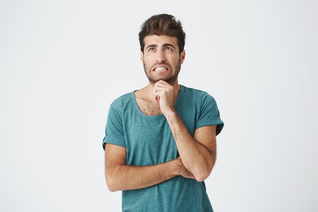 Portret van ongelukkige jonge blanke man in blauw t-shirt, met een goed kapsel en baard, met een extreem bang uitdrukking denken over het overslaan van de lezing van boze leraar.