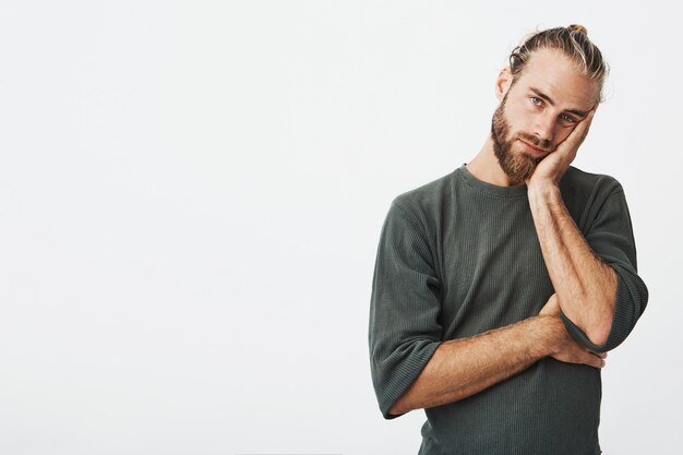 Portret van ongelukkige volwassen bebaarde man in grijs shirt met hand op uitgeput en moe wang