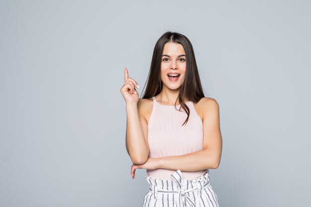 Portret van opgewonden jonge vrouw wees met vinger omhoog geïsoleerd over grijze muur heeft een idee.