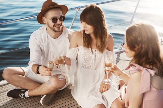 Portret van paar en hun vriend, zittend op jacht terwijl drinken en tijd vrolijk doorbrengen. volwassene nippen champagne in trendy kleding terwijl hij op luxe vakantie