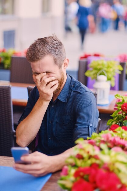 Portret van positieve roodharige bebaarde man met behulp van een smartphone.