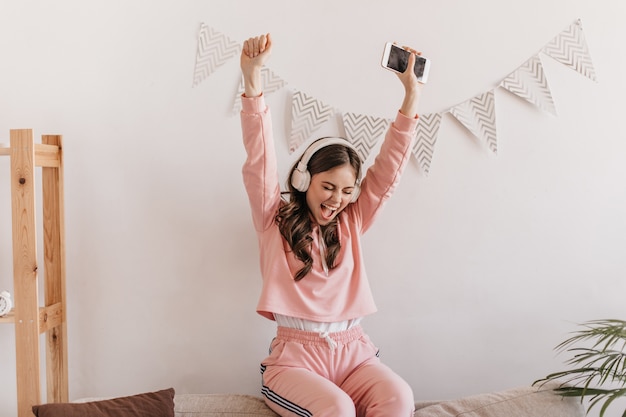 Portret van positieve vrouw in roze sweatshirt vreugdevol handen opheffen