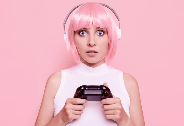 Portret van prachtige gelukkig gamer meisje met roze haren spelen van videospellen met joystick op kleurrijk in studio Gratis Foto