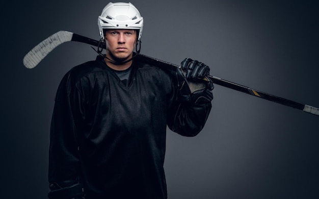 Portret van professionele hockeyspeler houdt gaming stick geïsoleerd op een grijze achtergrond.