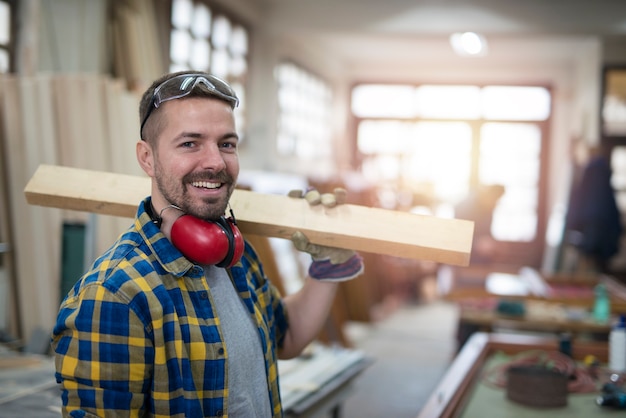Portret van professionele timmerman van middelbare leeftijd met houten plank en hulpmiddelen die zich in zijn workshop houtbewerking bevinden