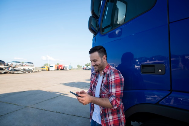Portret van professionele vrachtwagenchauffeur van middelbare leeftijd die zich door zijn vrachtwagen bij vrachtwagenstop bevindt die tabletcomputer gebruikt