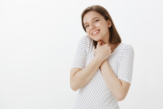 Portret van romantische en tedere leuke vrouw drukt handen op de borst en lacht schattig