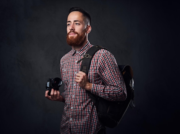 Portret van roodharige bebaarde freelancer fotograaf houdt een digitale camera over grijze achtergrond.