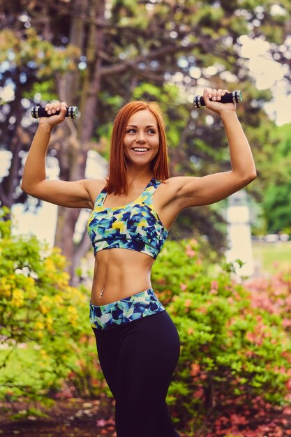 Portret van roodharige fitness vrouw houdt halters in een openlucht park.