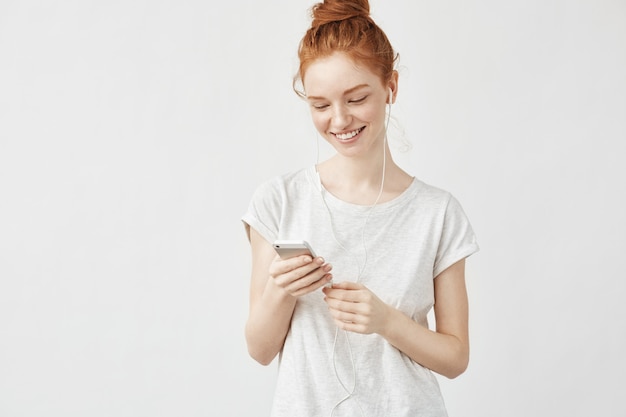 Portret van roodharigevrouw glimlachen die telefoon bekijken.