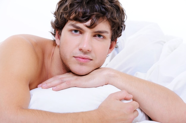 Gratis foto portret van rustige man met een knap gezicht liggend in bed met kussen