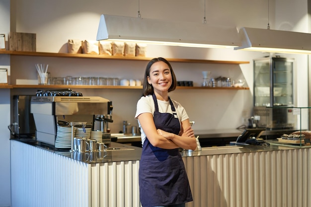 Portret van schattig aziatisch vrouwenbarista-cafépersoneel dat zich in de buurt van de toonbank bevindt met een koffiezetapparaat met ap