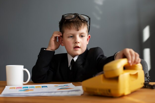 Portret van schattig kind in pak met behulp van roterende telefoon op kantoor