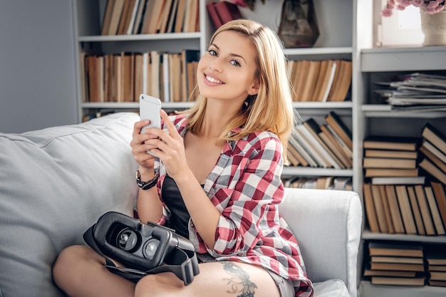 Portret van schattige blonde vrouw met behulp van smartphone en virtual reality-bril.