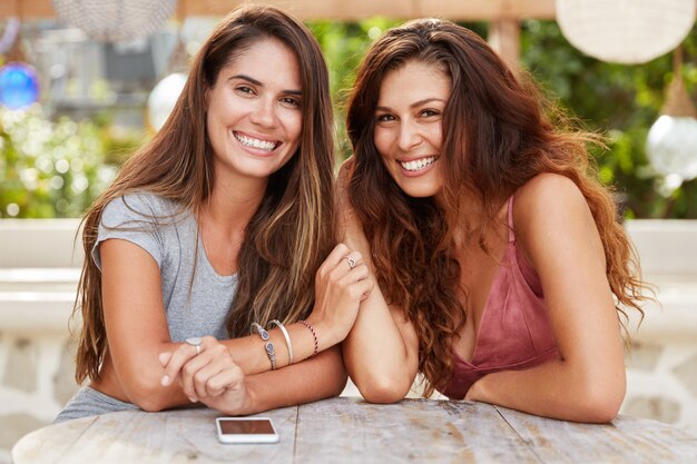 Portret van schattige brunette vrouw ontmoeten elkaar in cafetaria, omgeven door slimme telefoon, hebben een aantrekkelijk uiterlijk